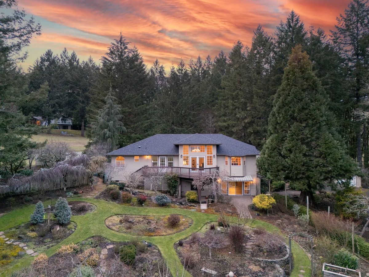 A Corvallis hillside home at dusk, lit from within, above terraced gardens, from one of Marty Fulford's listings
