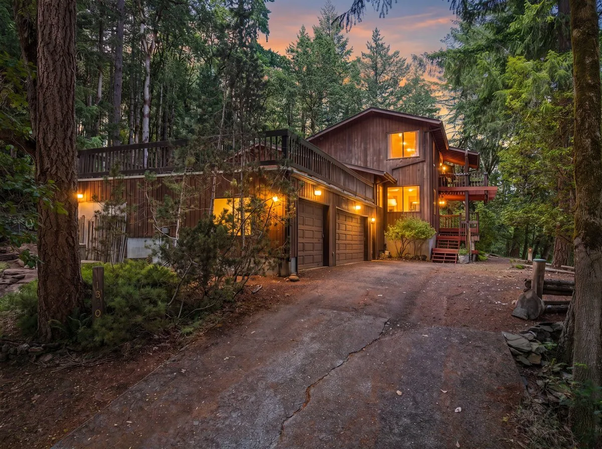 A cedar-sided home in the woods on Magnolia Drive in Corvallis at dusk, windows lit from within, from one of Marty Fulford’s listings
